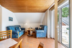 Une pièce comprenant deux canapés à motifs, une table en bois, une petite table d’appoint ronde et une grande porte-fenêtre coulissante donnant sur un espace extérieur.