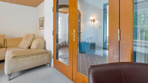 A room with a sofa, a wooden door, and a view of a bathroom with a blue cabinet. - Apartment 'Obendrot' with Shared Terrace, Shared Garden and Wi-Fi (Nordstrand)