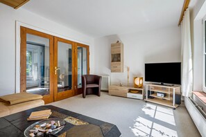 A living room with a sofa, a coffee table with stones, a TV on a stand, a wooden cabinet, and a sliding glass door.