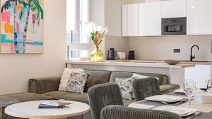 A modern living room with a sofa, a round coffee table, and a dining area with chairs and a table set for two.