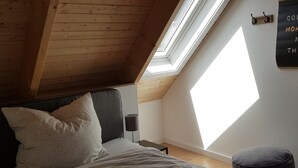 Una camera da letto con soffitto a falde, un lucernario, un letto con biancheria a motivi, una lampada da comodino e un cartello fissato alla parete.