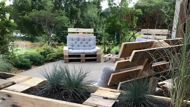 A wooden deck with a cushioned seating area, surrounded by greenery and trees. - Apartment 'Wanderlust' with Private Terrace, Private Garden and Wi-Fi (Heide)