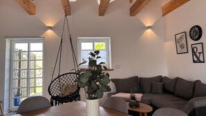 A modern living room with a wooden ceiling, a sofa, a dining table, and a hanging chair. - Apartment 'Wanderlust' with Private Terrace, Private Garden and Wi-Fi (Heide)