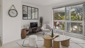 Un salon moderne doté d’une grande fenêtre, d’un téléviseur à écran plat, d’un fauteuil blanc et d’une table basse ronde.