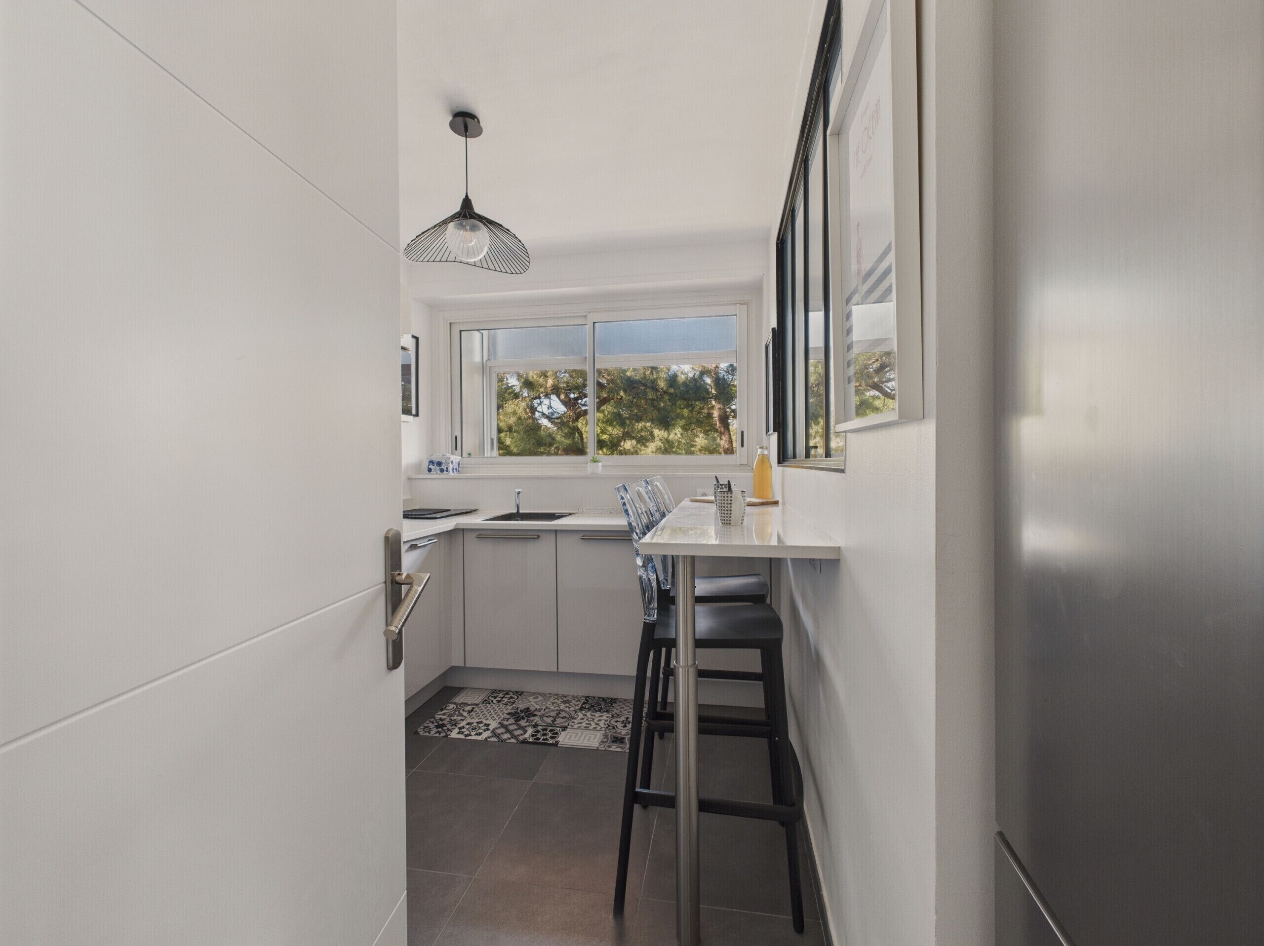 Une cuisine moderne avec une fenêtre, une table à manger et un luminaire noir suspendu au plafond.