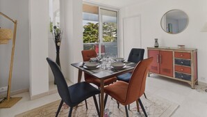 Un coin repas avec une table dressée pour quatre personnes, un buffet rouge avec des tiroirs et une grande fenêtre donnant sur les arbres.