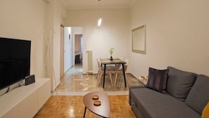 A modern living room with a flat-screen TV, a sofa, a dining table with chairs, and a hallway leading to a bedroom. - Charming Kallithea Apt, fully Reno, Fully Equipped (Kallithea)