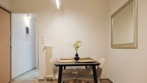 A dining area with a table, chairs, a vase with flowers, a radiator, and a mirror on the wall. - Charming Kallithea Apt, fully Reno, Fully Equipped (Kallithea)