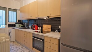 A modern kitchen with wooden cabinets, a stainless steel refrigerator, and a black tiled backsplash. - Charming Kallithea Apt, fully Reno, Fully Equipped (Kallithea)