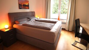 A double bed with a headboard, bedside tables with lamps, a desk, and a window with curtains.