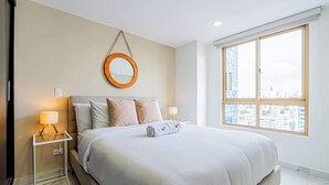 Ein Hotelzimmer mit einem großen Bett, einem runden Spiegel an der Wand, einem Nachttisch mit Lampe und einem Fenster mit Blick auf die Stadt.