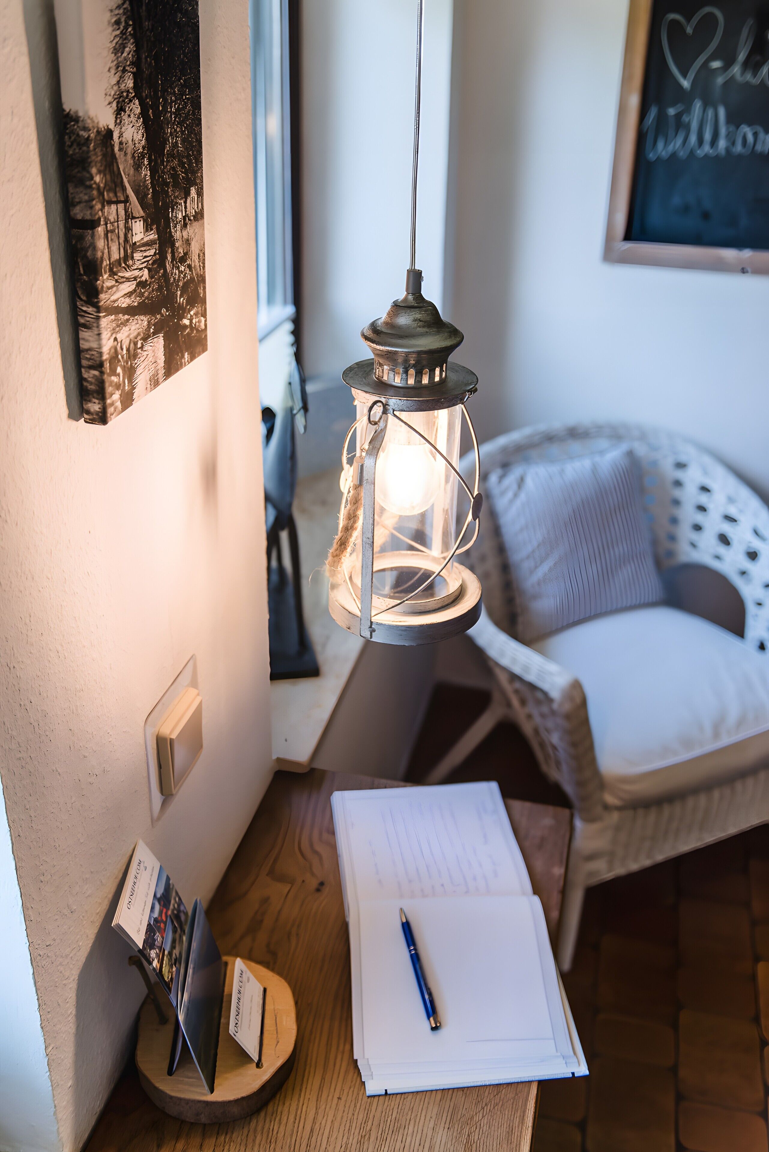 Ein gemütliches Zimmer mit einem Holztisch, einer hängenden Laterne, einem weißen Stuhl und einem an der Wand befestigten Bild.
