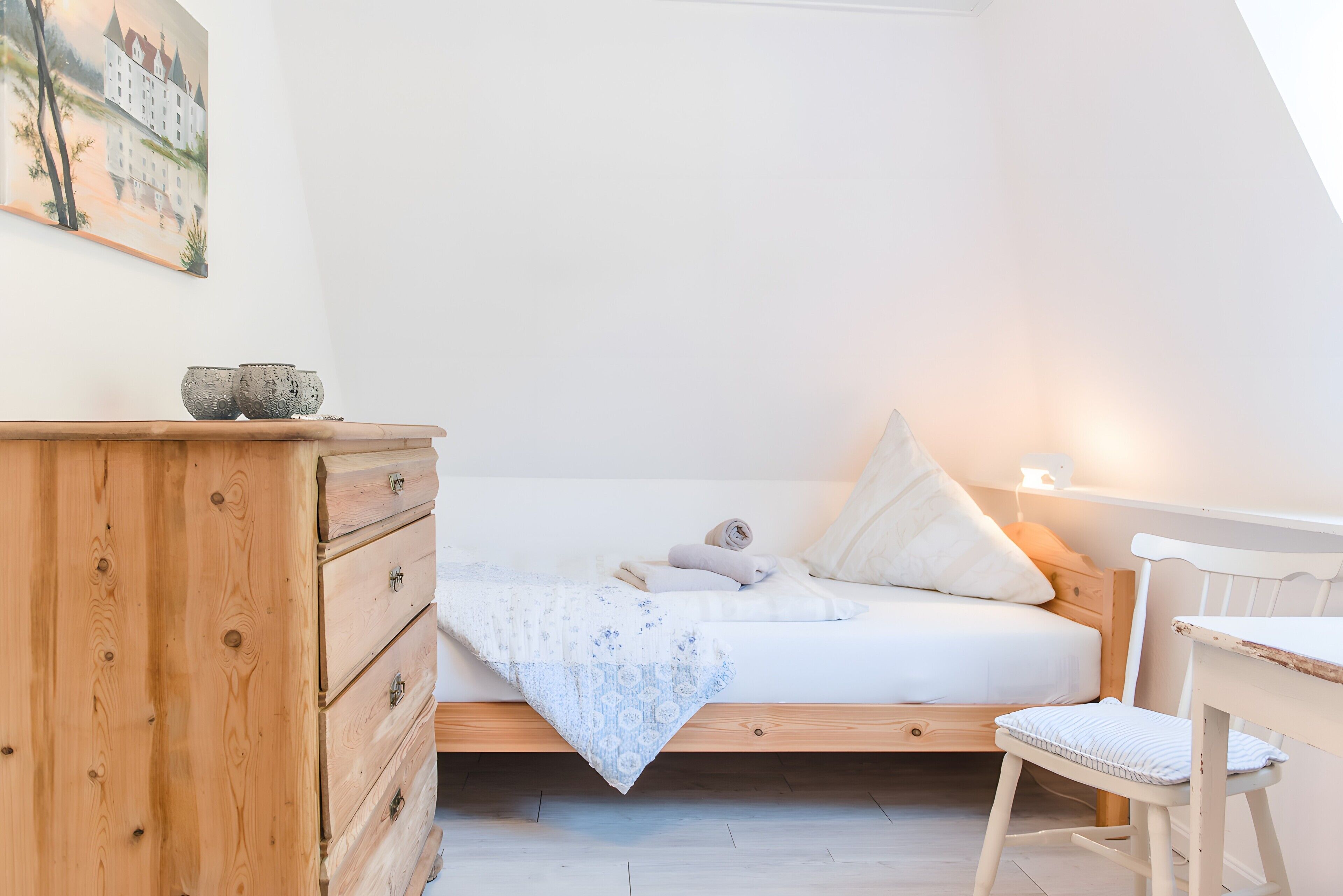 A bedroom with a bed, wooden dresser, and a desk with chair.