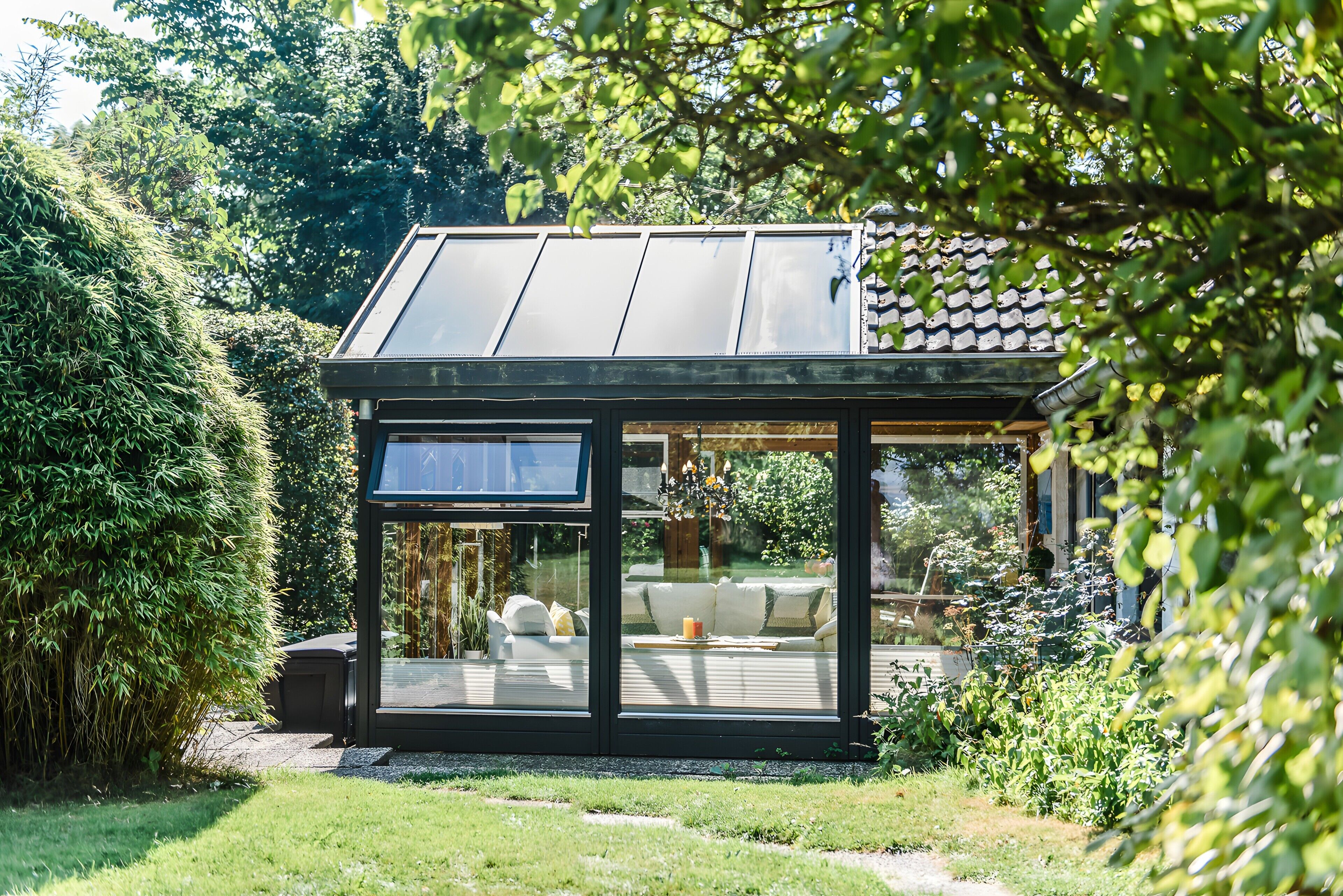 Eine moderne, verglaste Struktur mit Solardach, umgeben von üppigem Grün.
