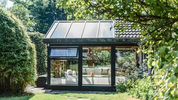 Eine moderne, verglaste Struktur mit Solardach, umgeben von üppigem Grün.