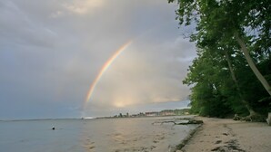 A beach with a rainbow, trees, and a distant shoreline. - Holiday Home 'Am Meer' with Sea View, Private Terrace and Wi-Fi (Langballig)
