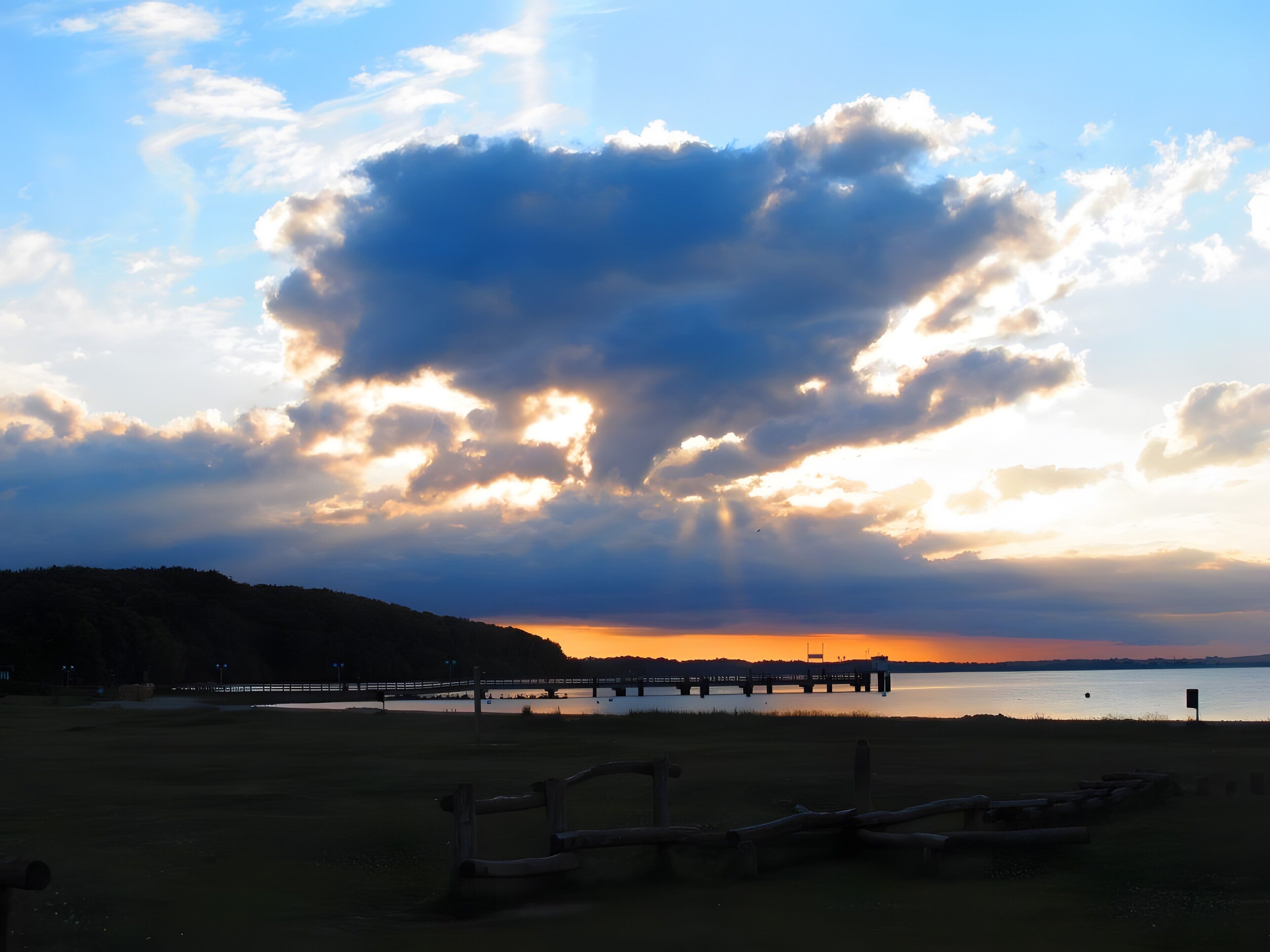 A beach with a wooden fence, a pier, and a cloudy sky.