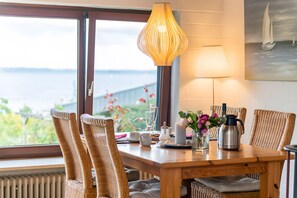 Una mesa de comedor con sillas de mimbre, una lámpara, un cuadro y vistas al mar.