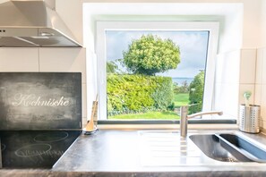 Una cocina con vista al jardín por una ventana, un lavamanos de acero inoxidable y una pizarra con texto.
