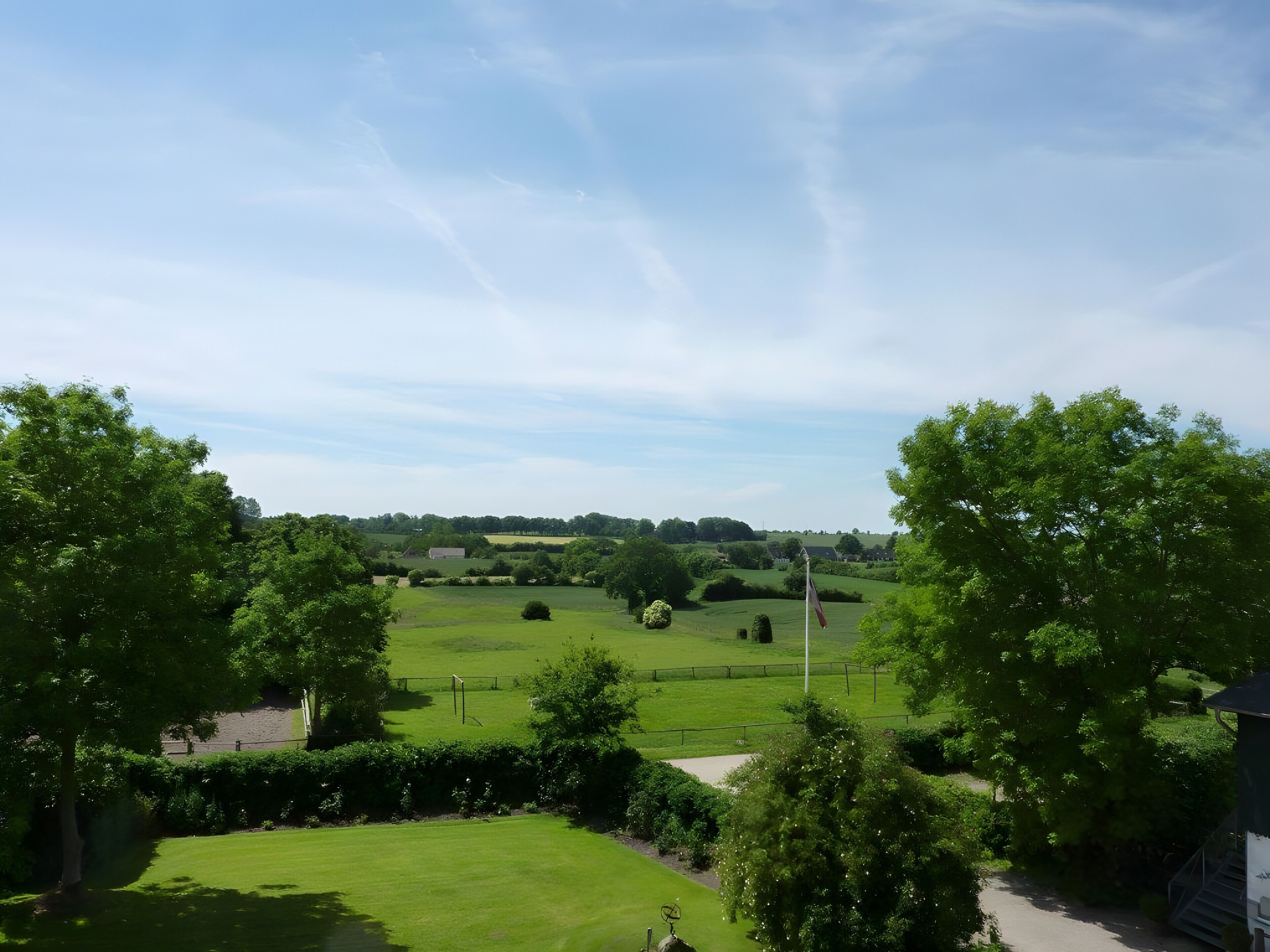 A rural landscape with a clear sky, green fields, and a flagpole.