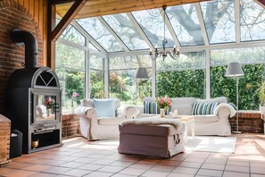 A sunroom with a brick fireplace, white furniture, and a large glass ceiling. - Holiday Home 'Hanghaus Am Meer' with Sea View, Private Terrace and Wi-Fi (Langballig)