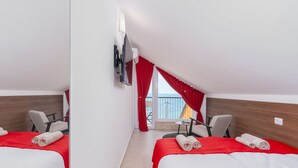 A hotel room with two beds, red curtains, a TV mounted on the wall, and a balcony with red curtains.