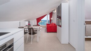 A modern apartment with a dining area, a red sofa, and a view of the sea.