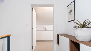 A hallway leading to a kitchen with white cabinets, a sink, and a framed picture on the wall.