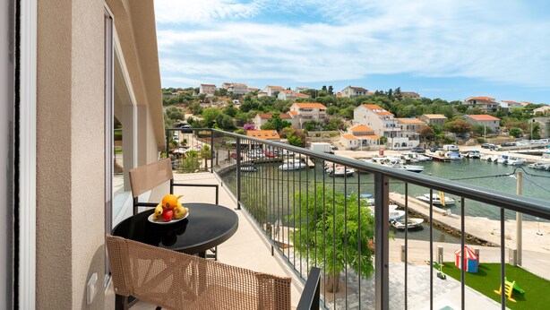 A balcony with wicker furniture, a table with fruit, and a view of a marina and buildings.