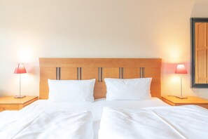 A double bed with two pillows, wooden headboard, two bedside lamps, and a wooden wardrobe.