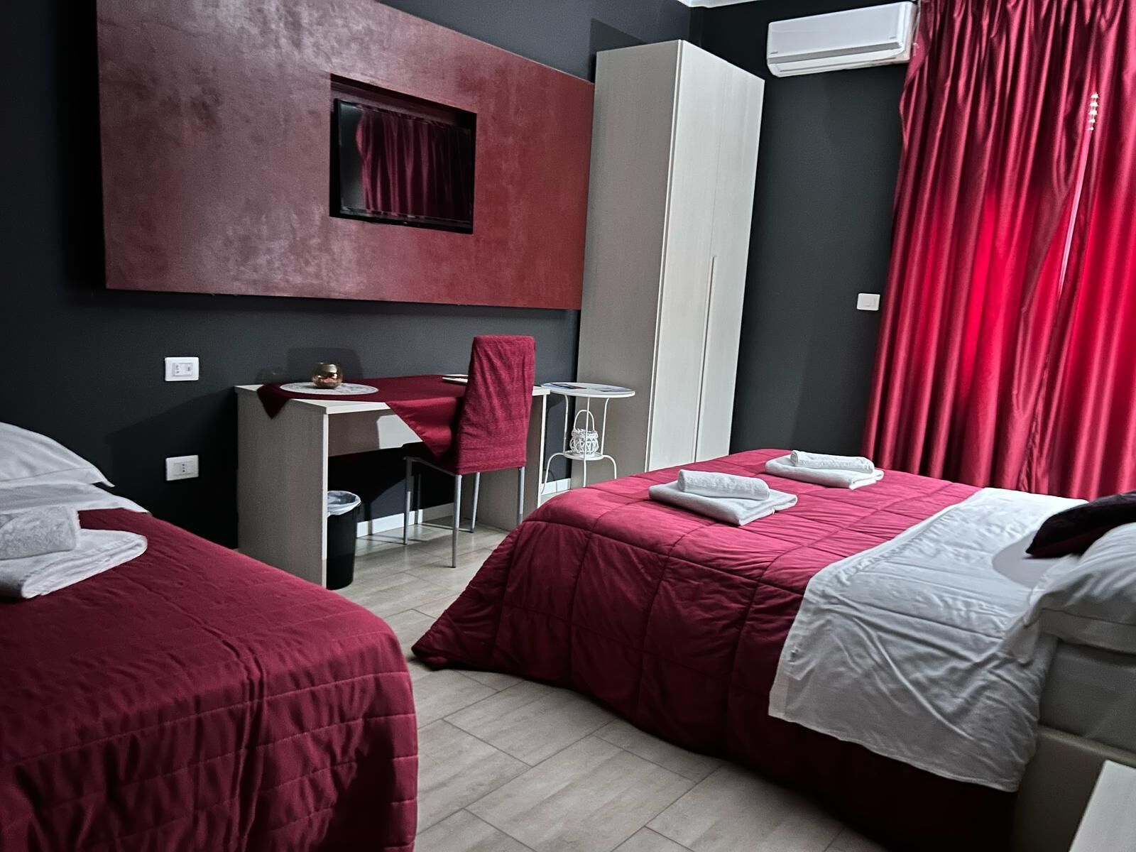 A hotel room with two beds, a desk, a chair, and a wardrobe.