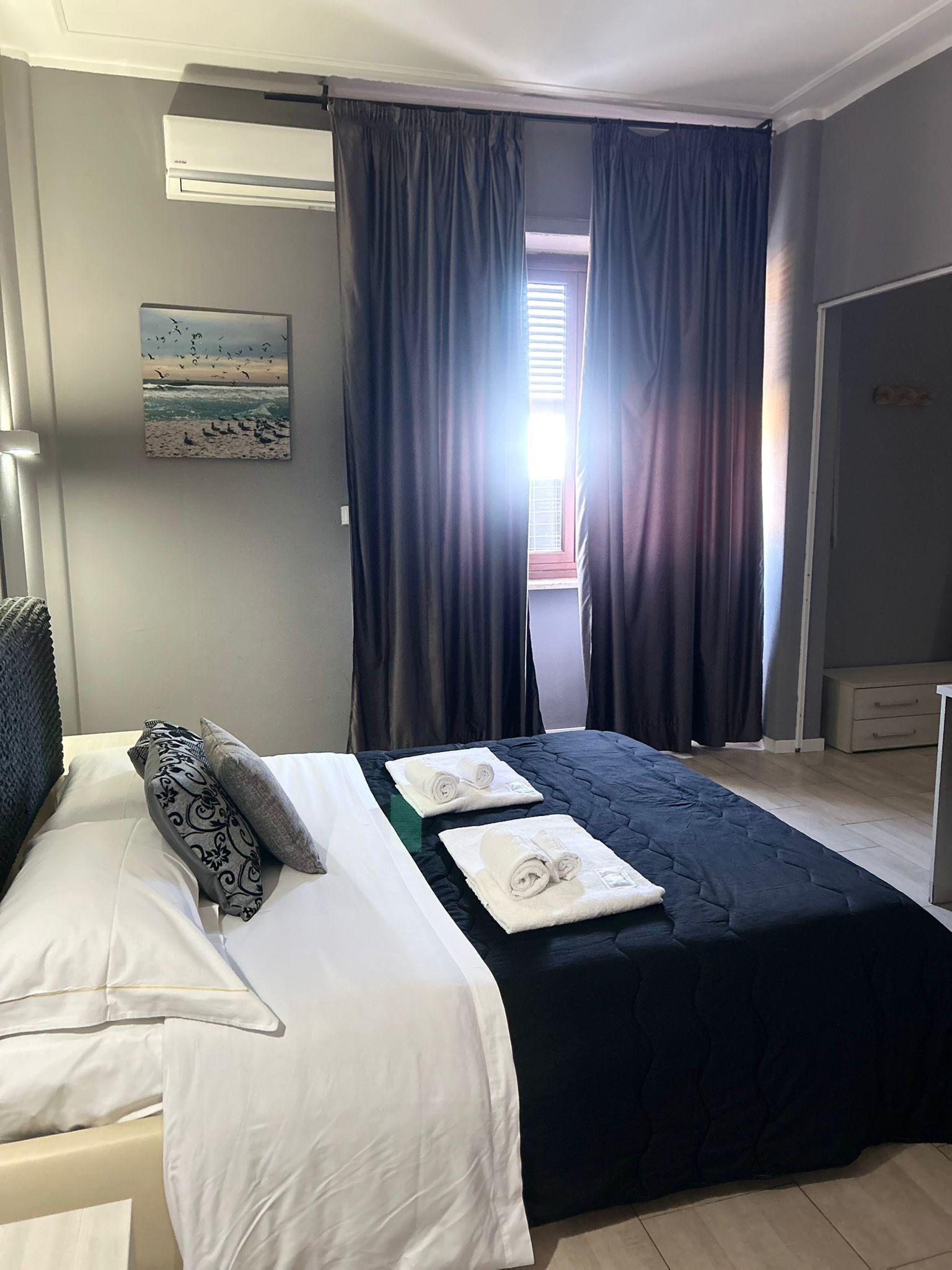 A hotel room with a bed, a painting, and a window with curtains.