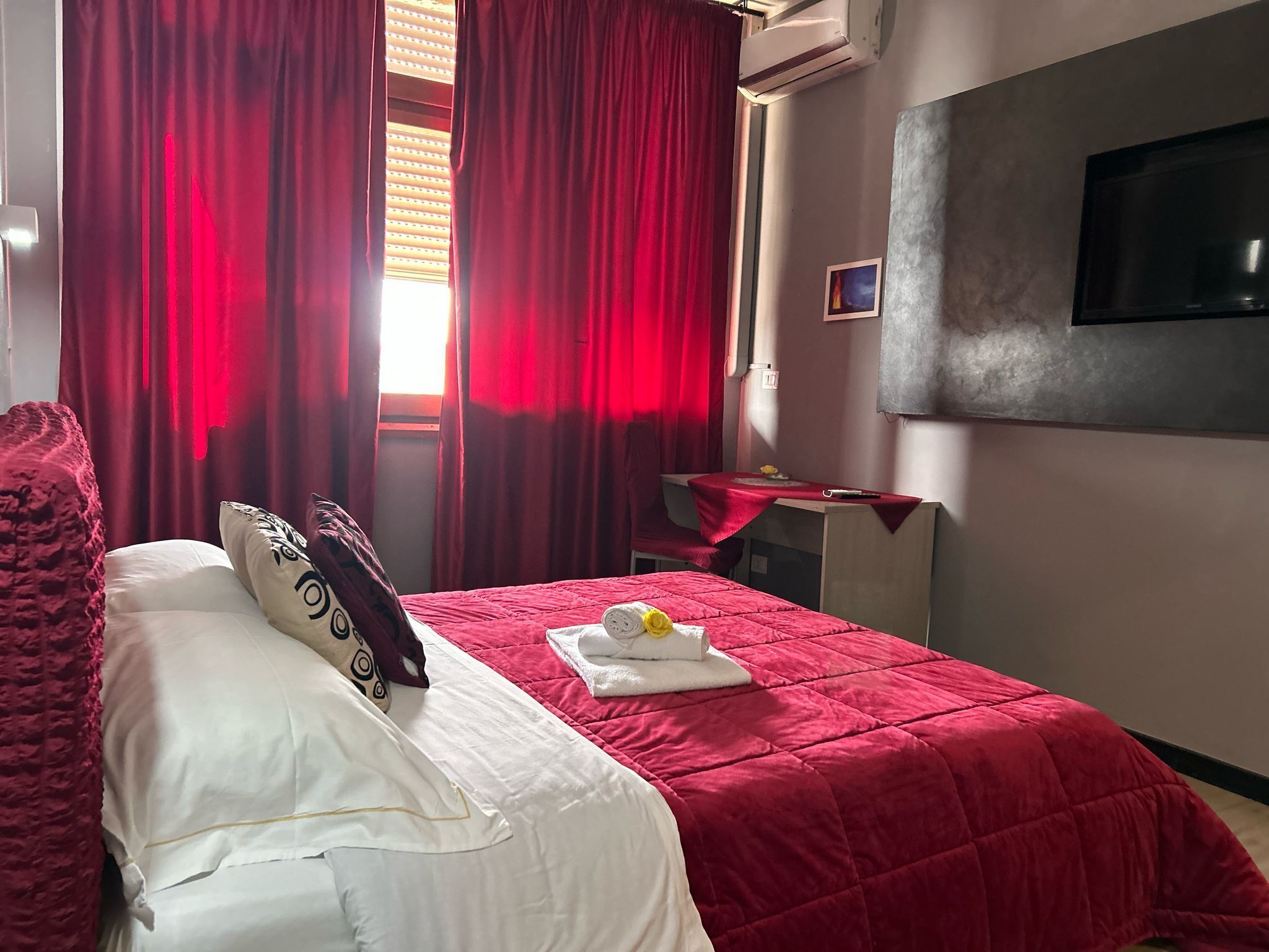 Una habitación de hotel con cama, cortinas rojas, un escritorio y una televisión de pantalla plana.