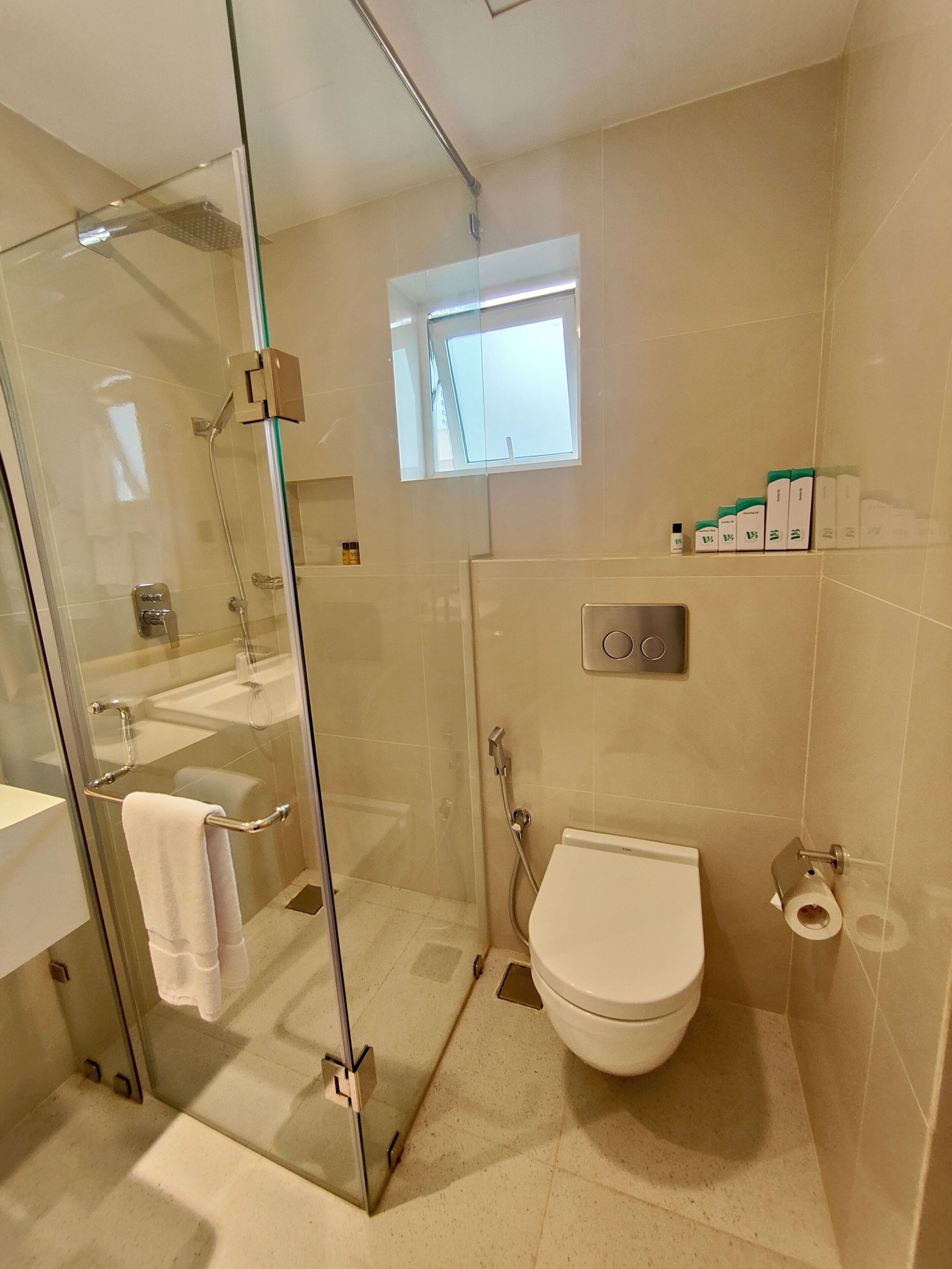 A modern bathroom with a glass shower enclosure, a toilet, and a small window providing natural light.
