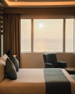 A hotel room with a bed, a chair, and a view of the sea through large windows. - Marine Bay Colombo (Colombo, Sri Lanka)