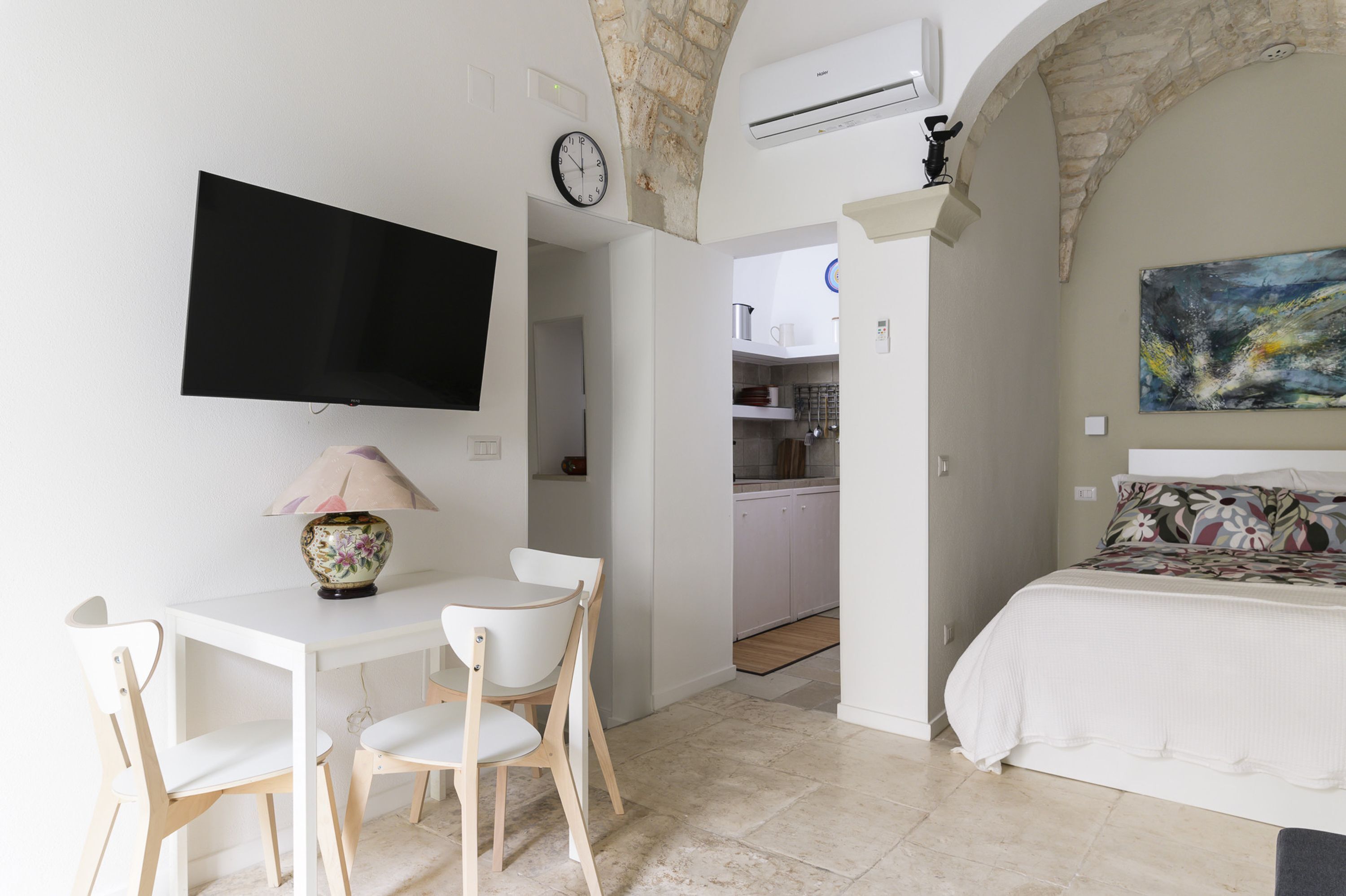 A bedroom with a bed, a TV mounted on the wall, a clock, and a painting.