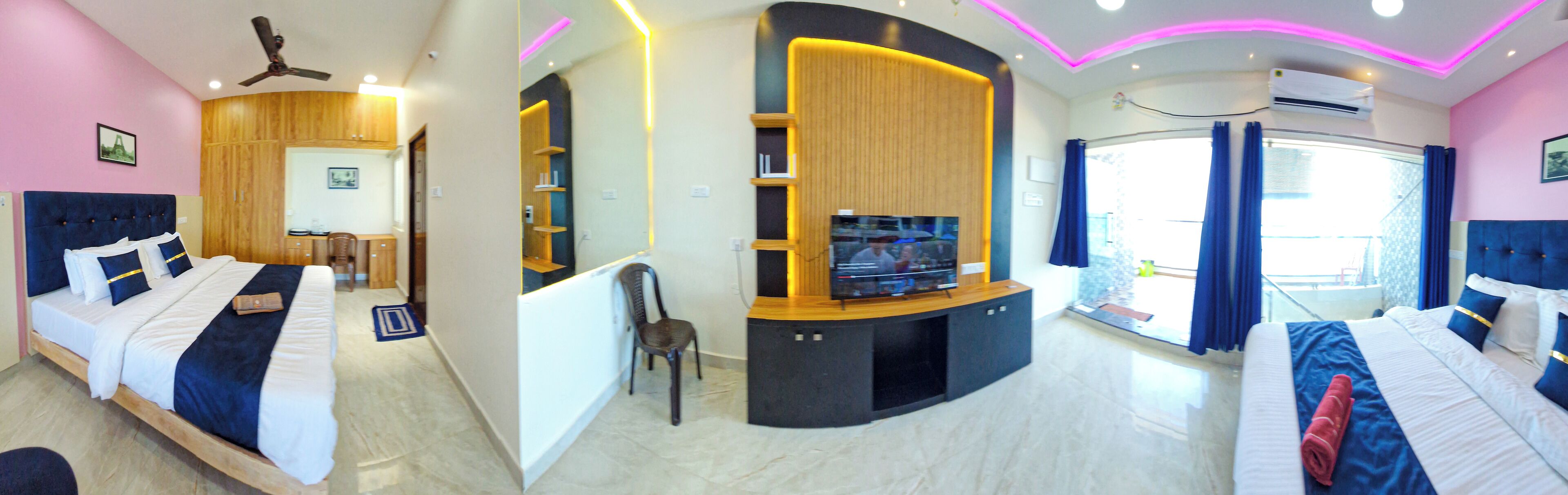 A modern hotel room with a curved bed, a TV, a small seating area, and a balcony with curtains.