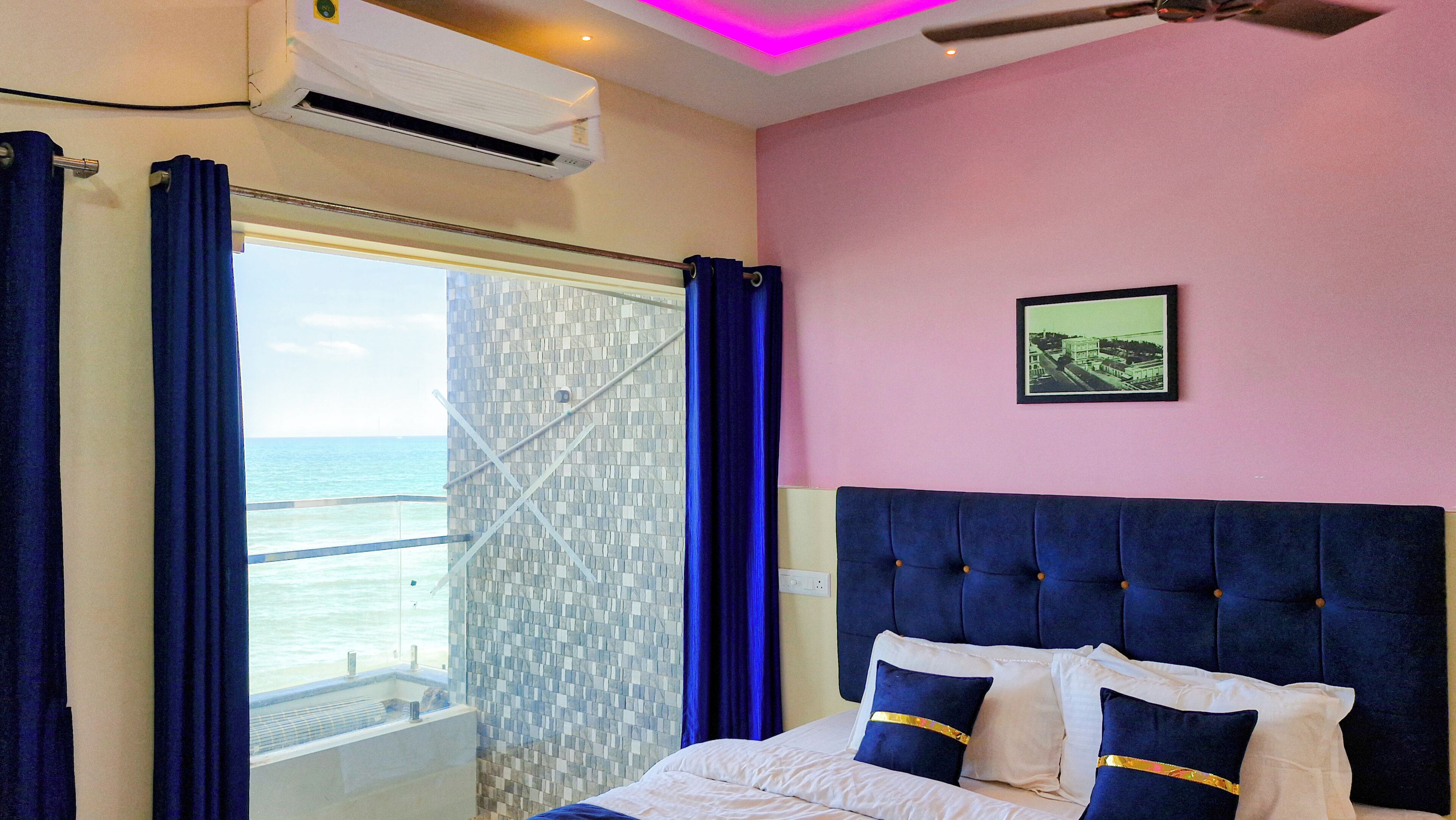 A bedroom with a view of the sea, a bed with blue headboard, and a picture on the wall.