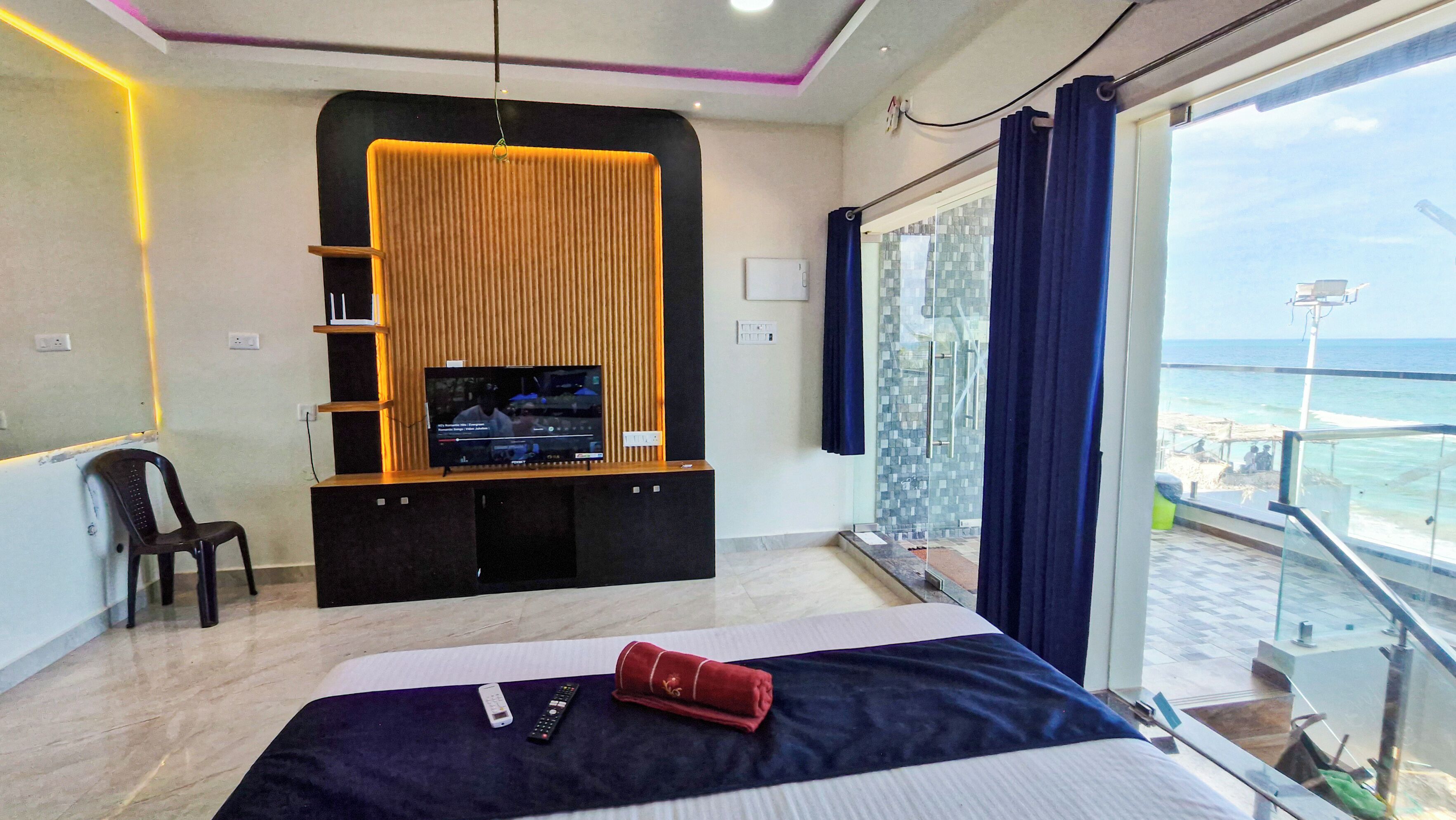 A hotel room with a bed, a TV on a wooden stand, a chair, and a view of the sea.