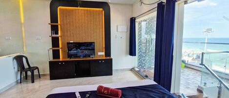 Ein Hotelzimmer mit Bett, Fernseher auf einem Holzboden, einem Sessel und Meerblick.