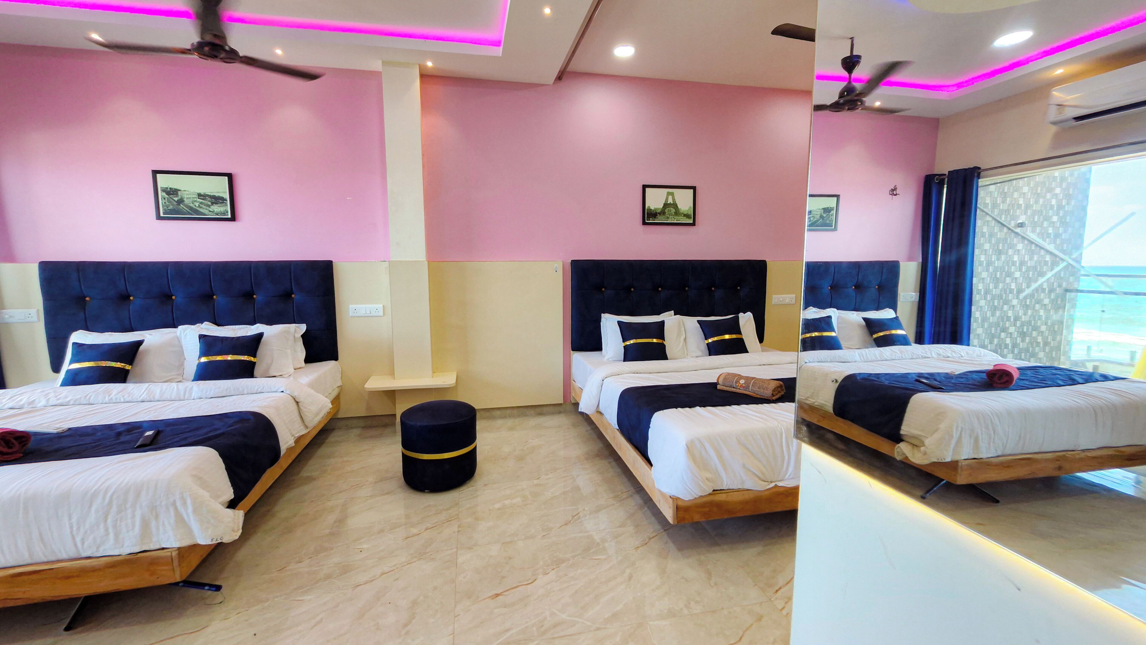 A hotel room with two beds, a small stool, a ceiling fan, and a window with curtains.