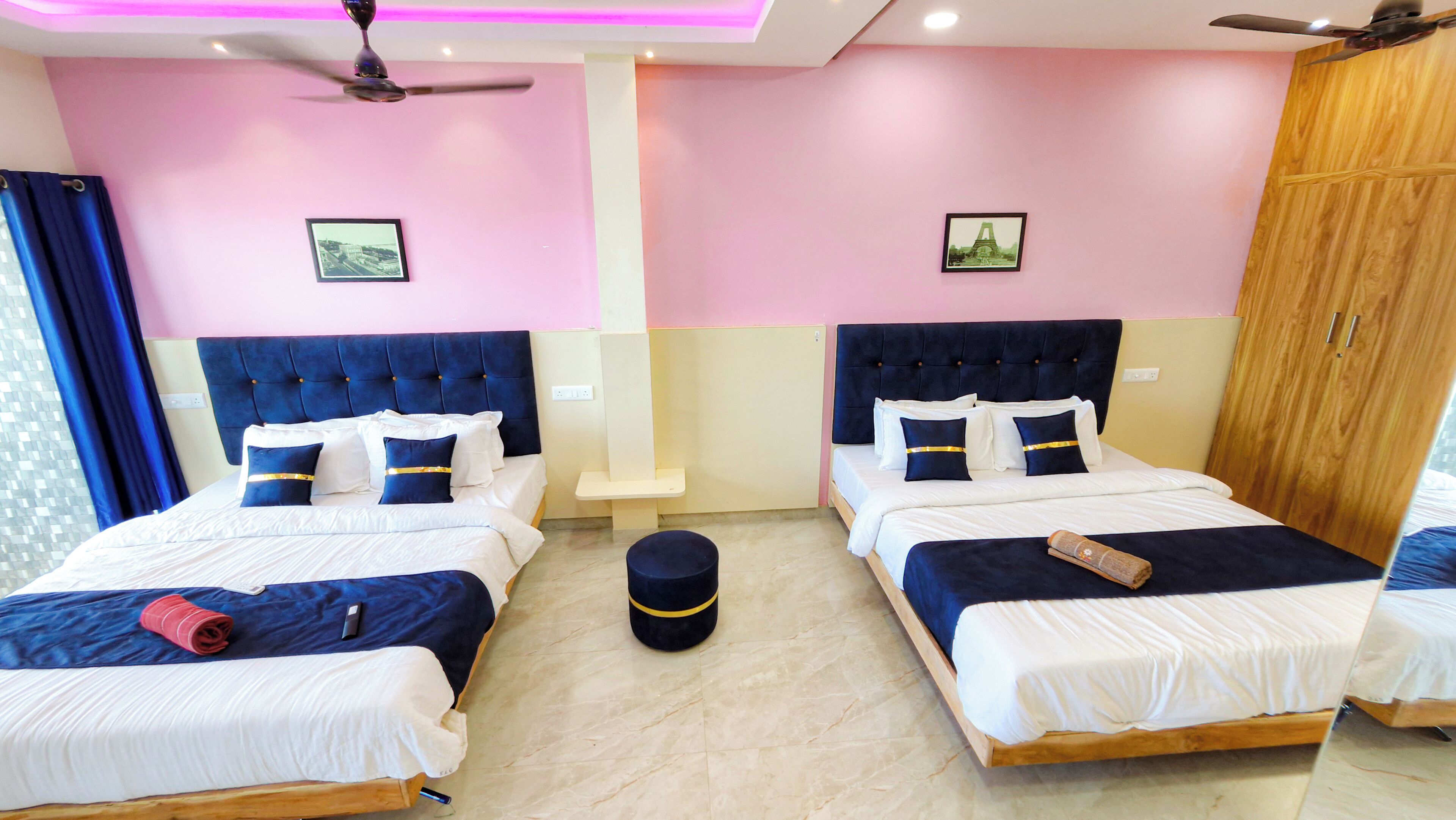A hotel room with two beds, a ceiling fan, and a small round ottoman.