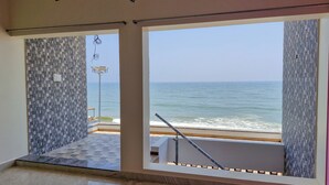 A room with a view of the sea through large windows, a tiled wall, and a metal railing.