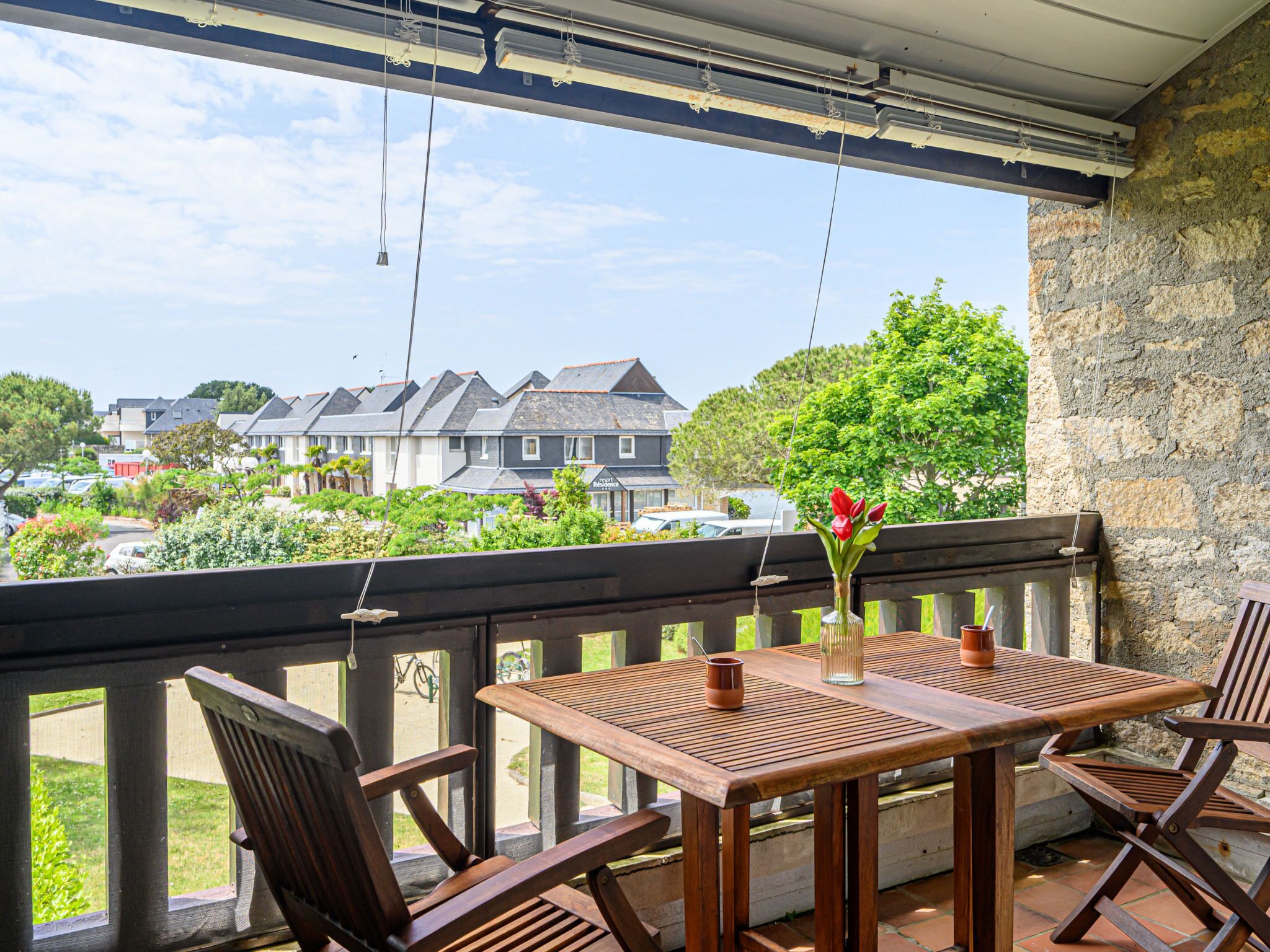 A wooden table and chairs on a balcony with a view of houses and greenery.