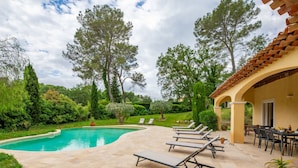 A pool area with lounge chairs and a patio table, surrounded by greenery and trees. - La Pimaleanne by Interhome (Roquefort les Pins)