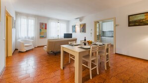 A spacious living area with a dining table set for four, a sofa, a TV, and a kitchen visible through an open door. - Lido Versilia by Interhome (Lido di Camaiore)