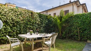 A patio with a table and chairs, surrounded by lush greenery and a house in the background. - Lido Versilia by Interhome (Lido di Camaiore)