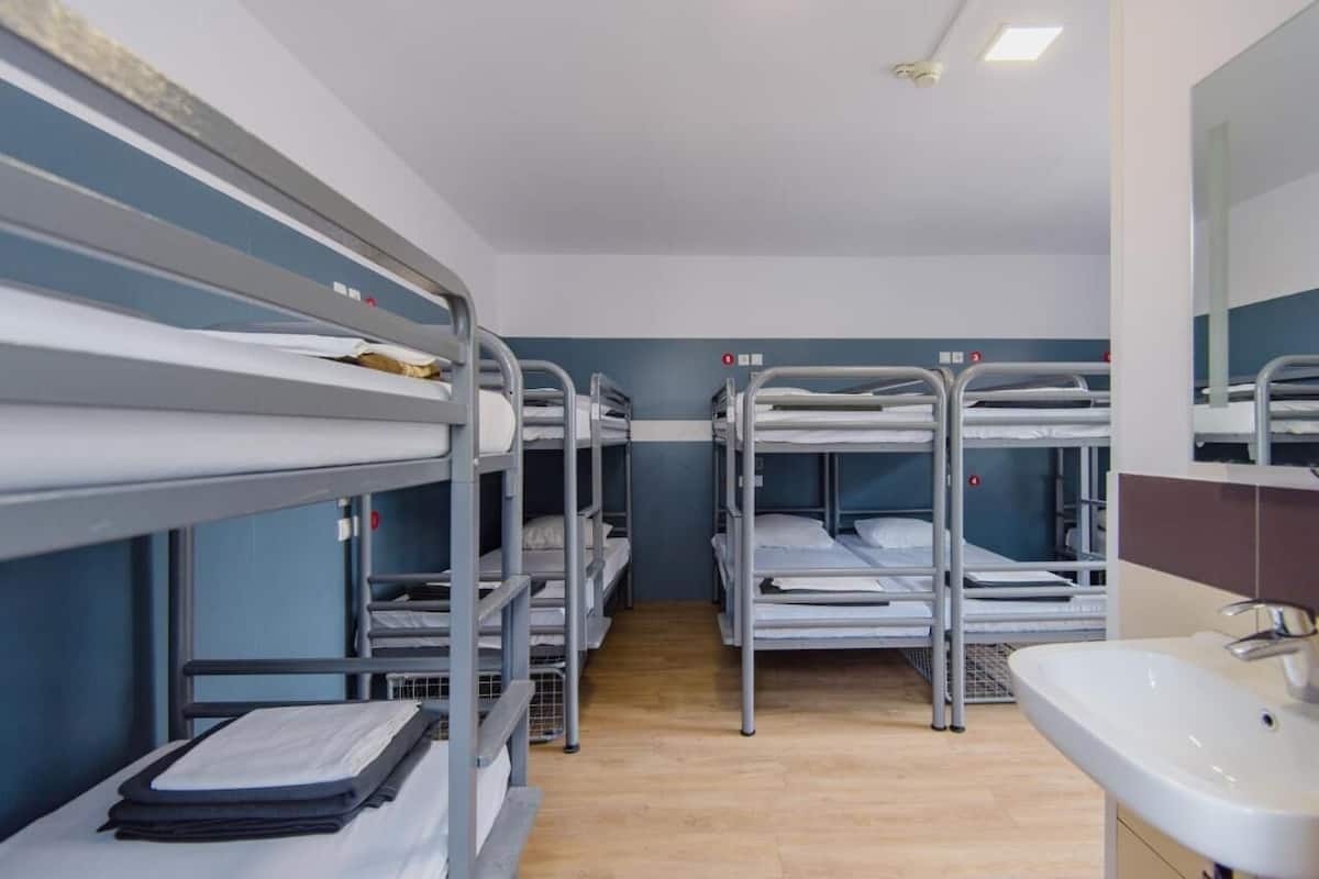Une chambre avec plusieurs lits superposés, un lavabo et un miroir.