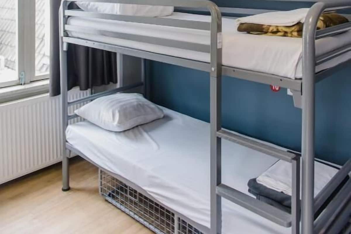 Une chambre avec un lit superposé, une fenêtre, des rideaux et un interrupteur fixé au mur.