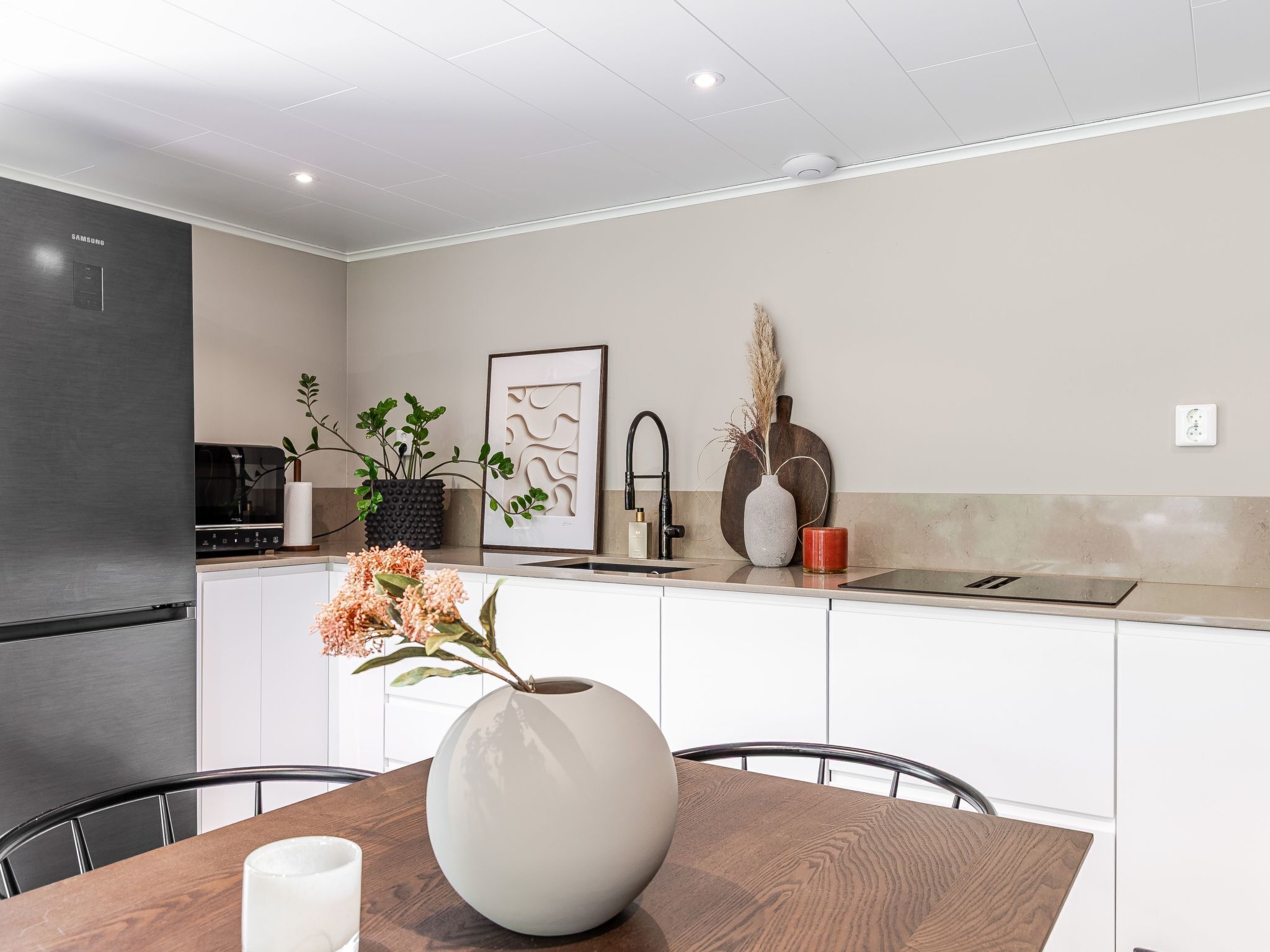 Een moderne keuken met witte kasten, een roestvrijstalen koelkast en een eethoek met een houten tafel en stoelen.